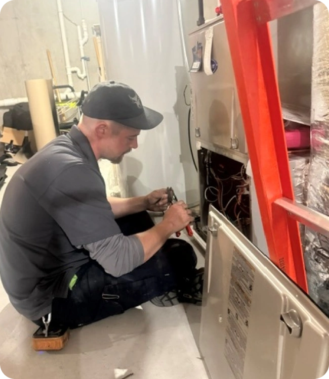 Caron Heating & Cooling technician repairing a furnace in a Massachusetts basement