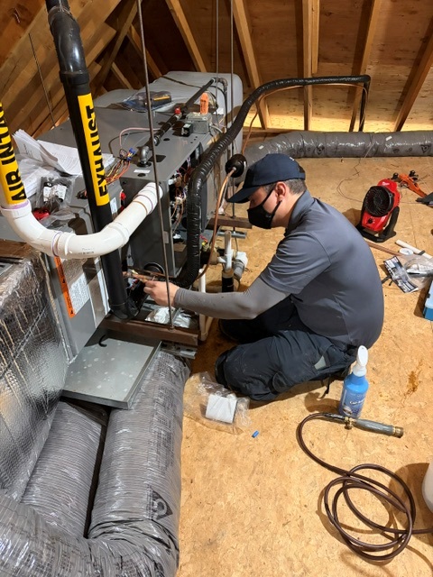 Caron Heating & Cooling technician installing a high-efficiency furnace in an attic