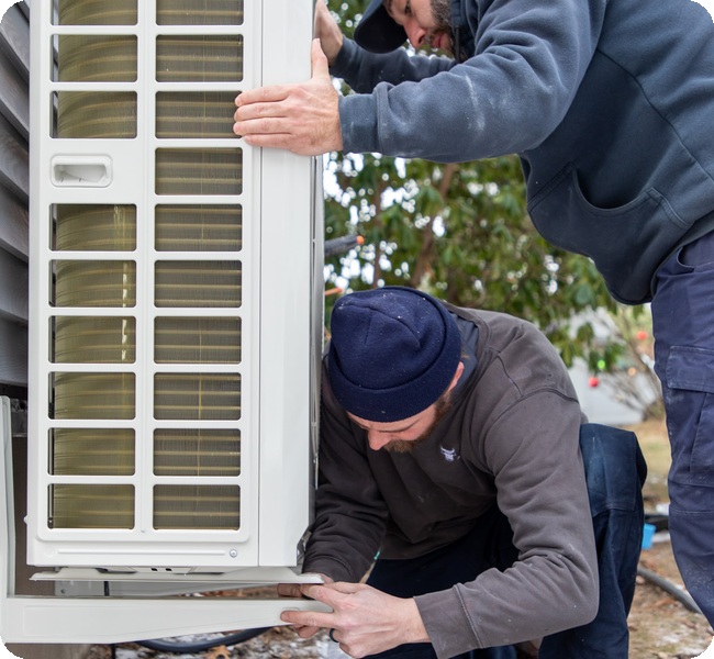 Caron technicians mounting a heat pump outdoor unit on its stand at a Merrimack Valley home
