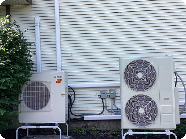 Two Mitsubishi heat pump outdoor units installed by Caron on the side of a Massachusetts home